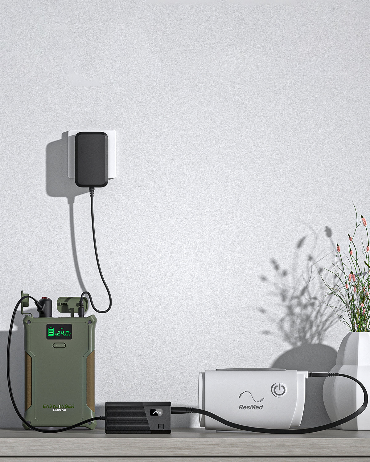 The EASYLONGER Universal CPAP DC Power Cord (12V/24V) charges a white ResMed device on a table near a potted plant, with the power cord plugged into a wall socket.