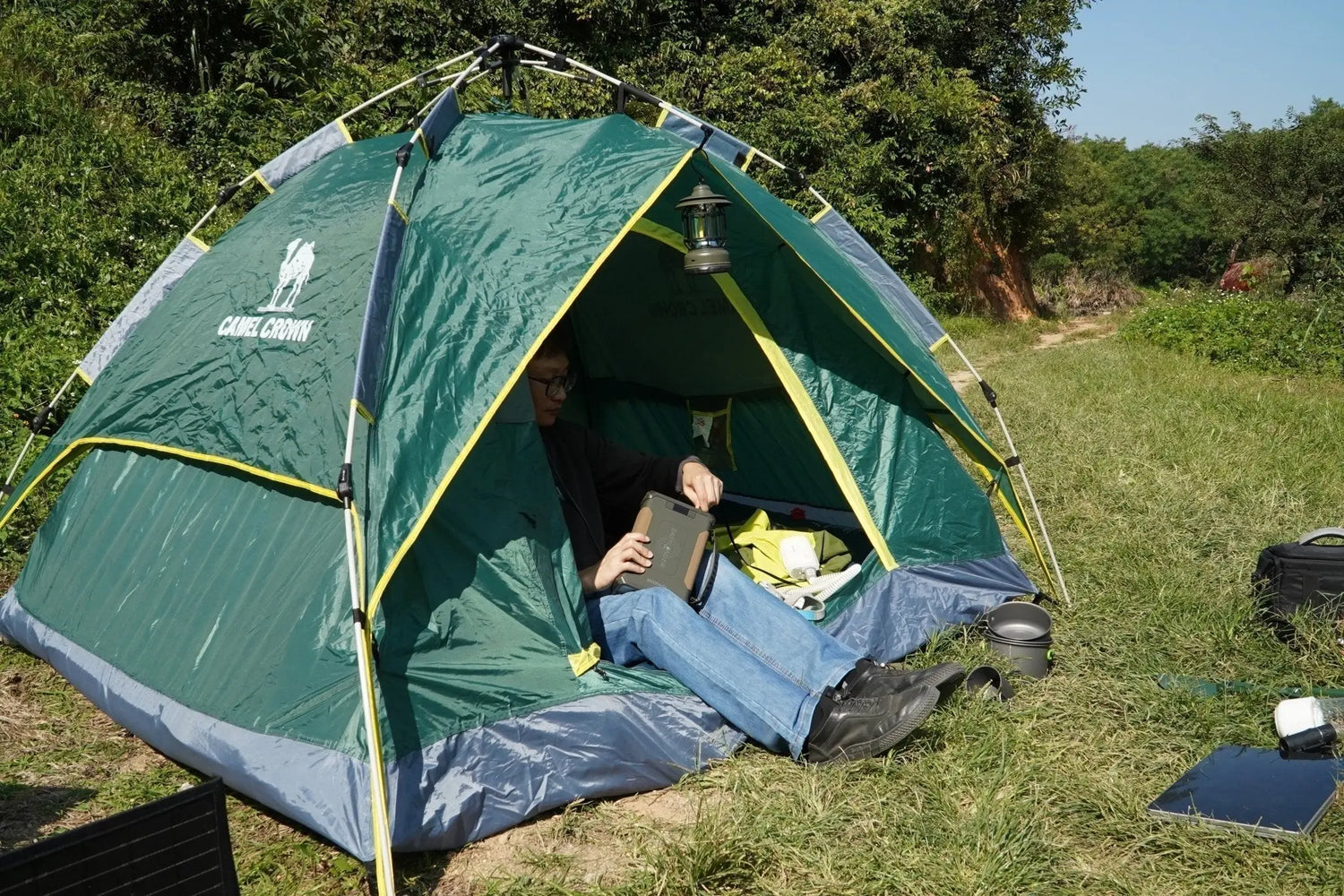 Person sitting in tent outdoors using ES400 AIR portable power station, camping gear visible