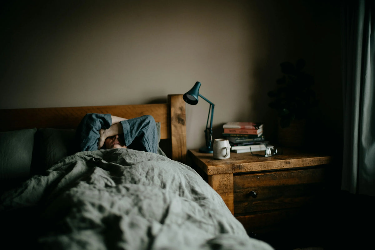Person awake in bed beside a nightstand and lamp
