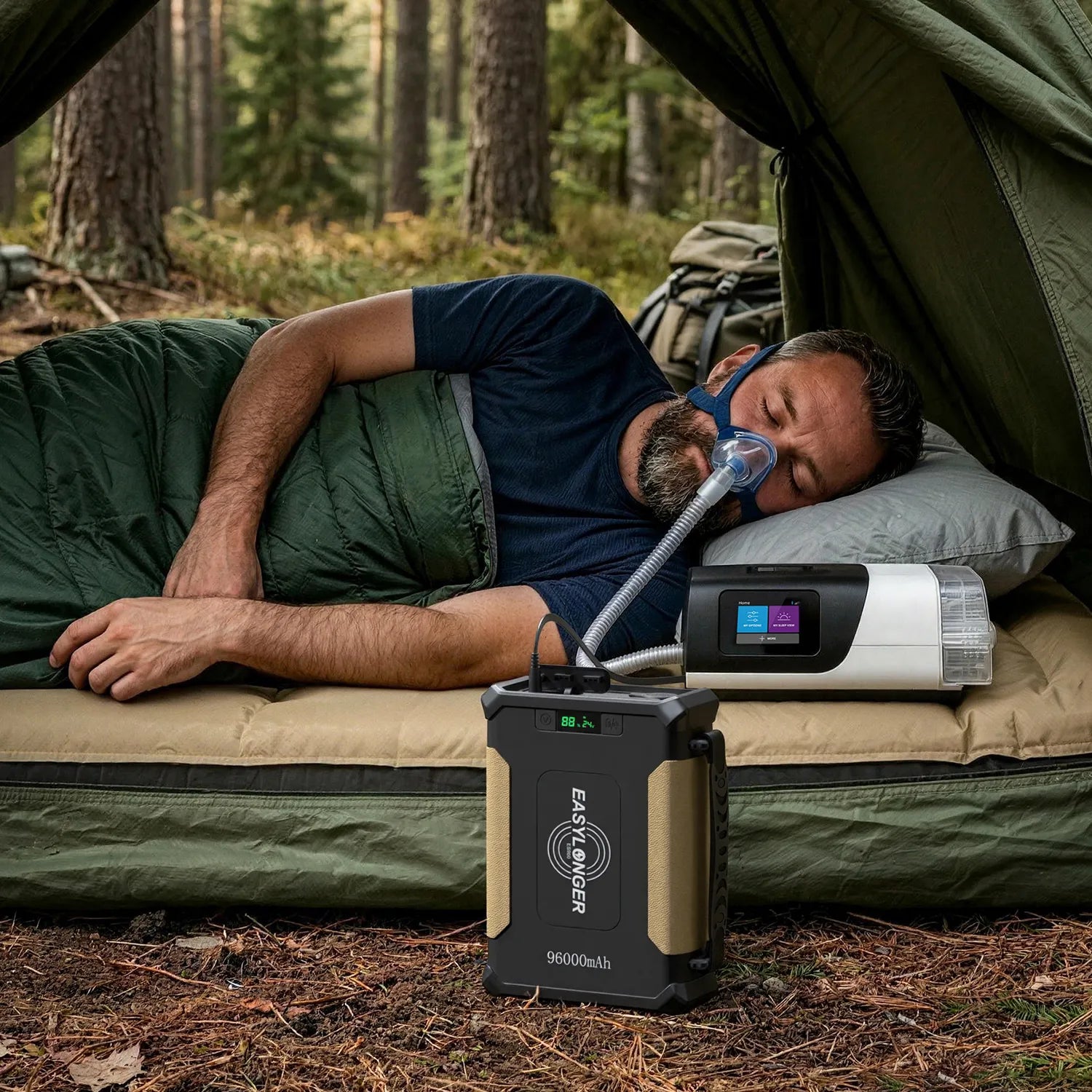A man sleeps in a tent inside a sleeping bag, using a CPAP machine connected to a portable power station. The tent is set up in a forested area.
